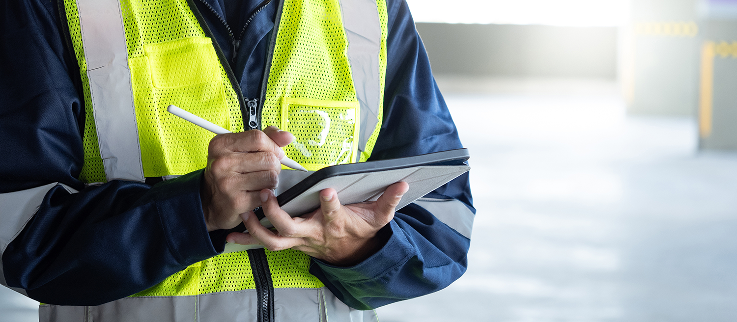An image of a person wearing a high-vis vest, holding a tablet and stylus