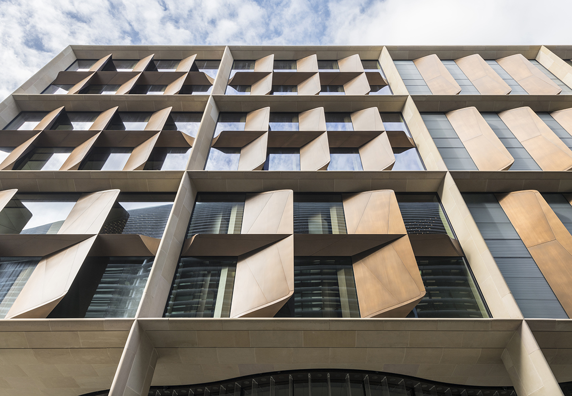 The building’s façades are defined by a deep structural stone frame with inset bronze fins and serrated glass